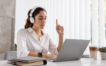 Student attending an online A Levels class on a laptop while wearing headphones and taking notes at a desk.